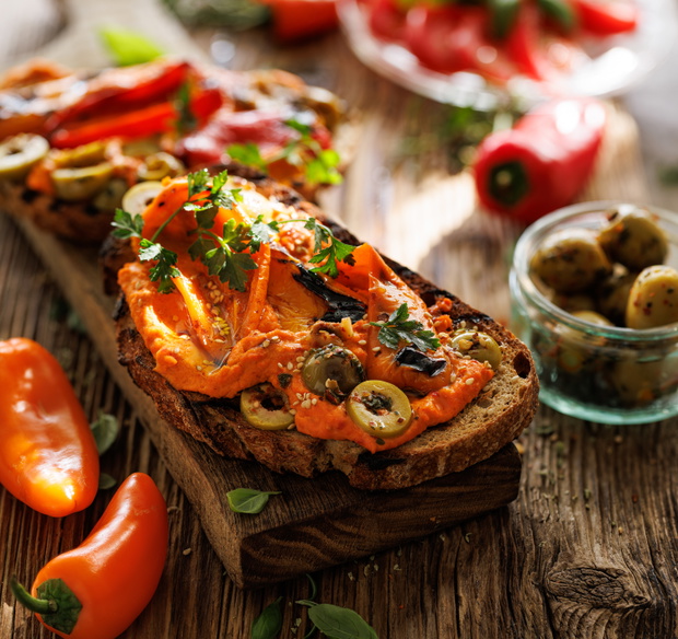 Close up view of sandwich from toasted traditional sourdough bread with hummus, grilled pepper and olives  sprinkled with fresh parsley on a wooden board