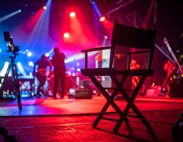 Director's chair on stage during a concert; red and blue stage lights.