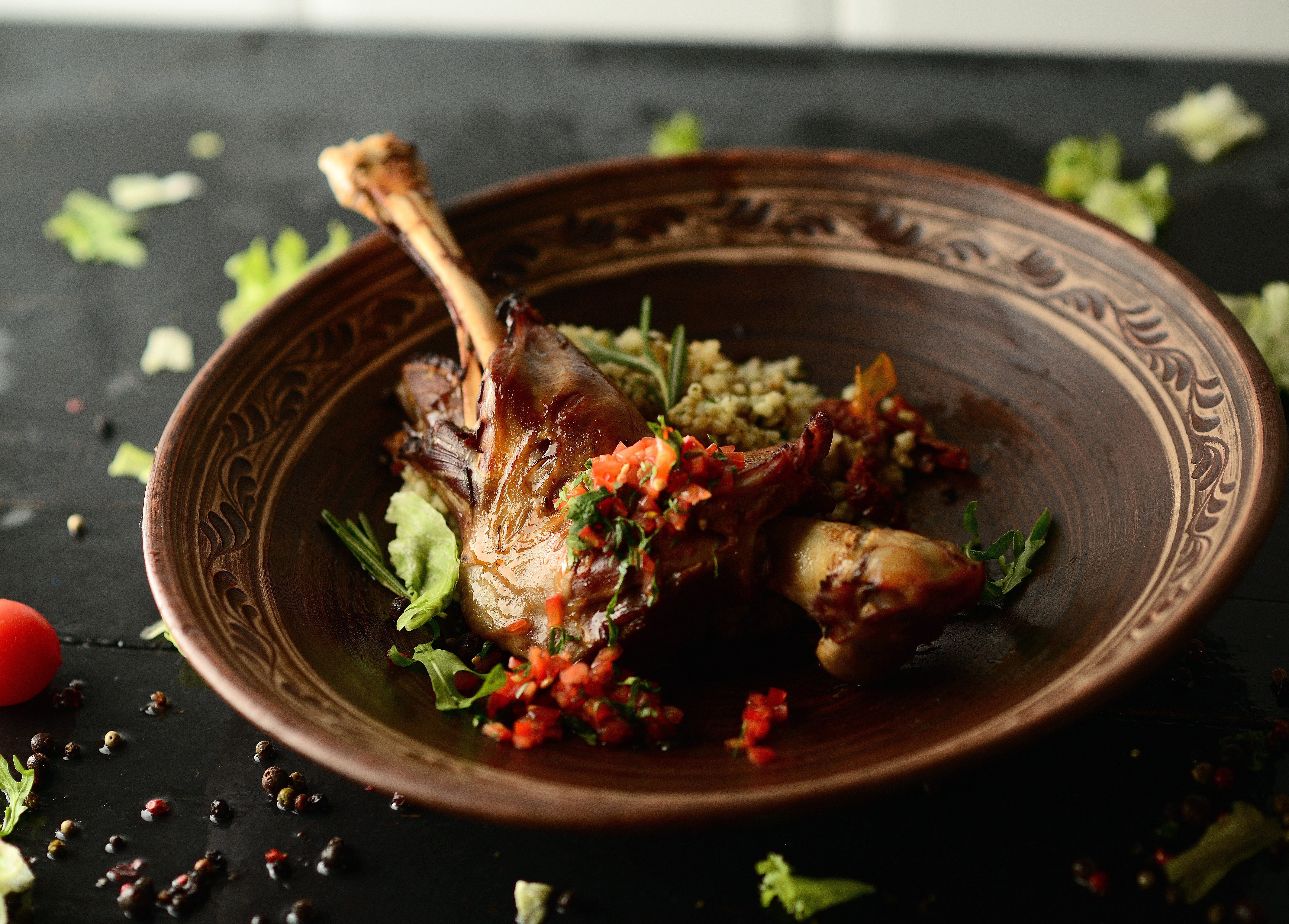 Roasted goose leg, sauce, herbs and tomatoes in a clay bowl on wooden background