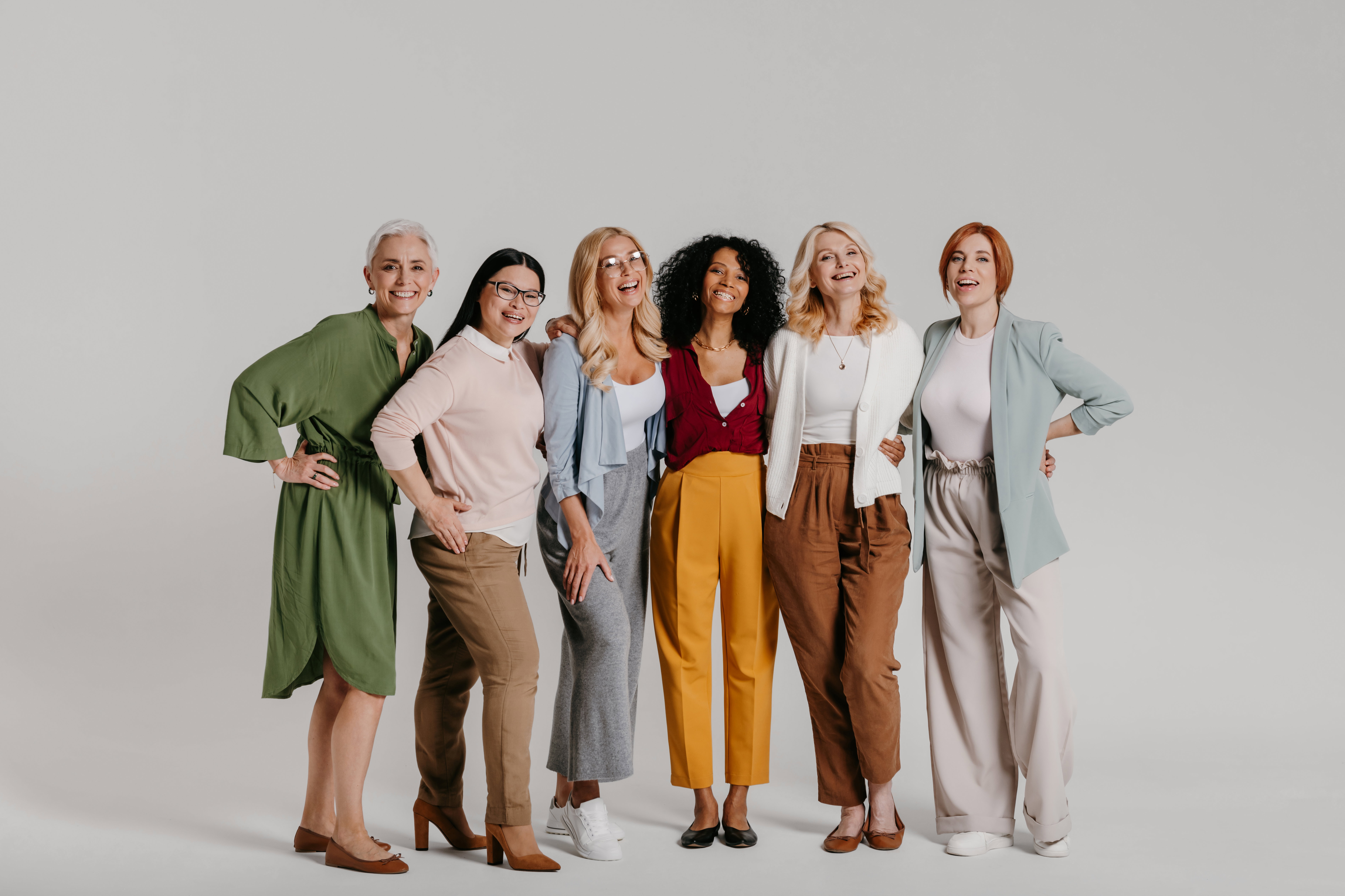Multi-ethnic group of happy mature women bonding against grey background