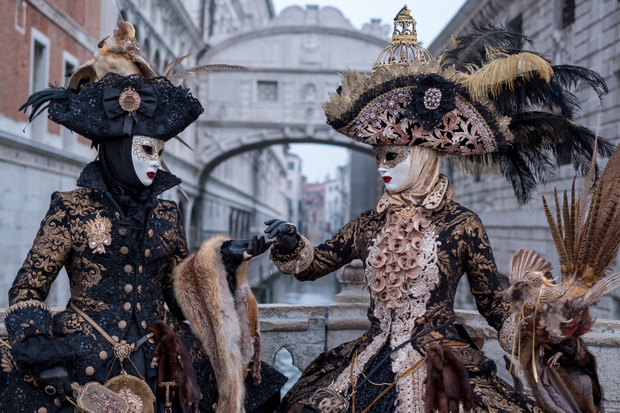 Venice Carnival: Two woman in costumes and masks, carrying feathered bird and birdcage