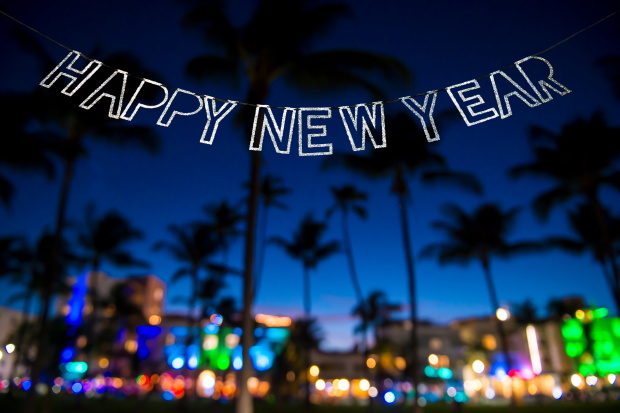 Happy New Year message hanging in glittery party bunting above tropical palm trees of the glowing neon lights of the skyline of Miami Beach, Florida, USA