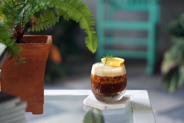 Iced coffee with orange - A glass of espresso shot mixed with craft soda and orange juice and topped with rosemary leaves on blurred background.