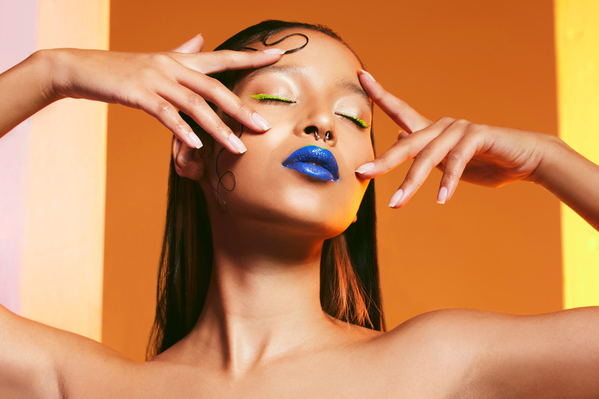 Blue lipstick, makeup and face of woman in studio for cosmetics, eye shadow and beauty salon. Creative aesthetic, cosmetology and female person pose with hands for glamour, luxury style and glow