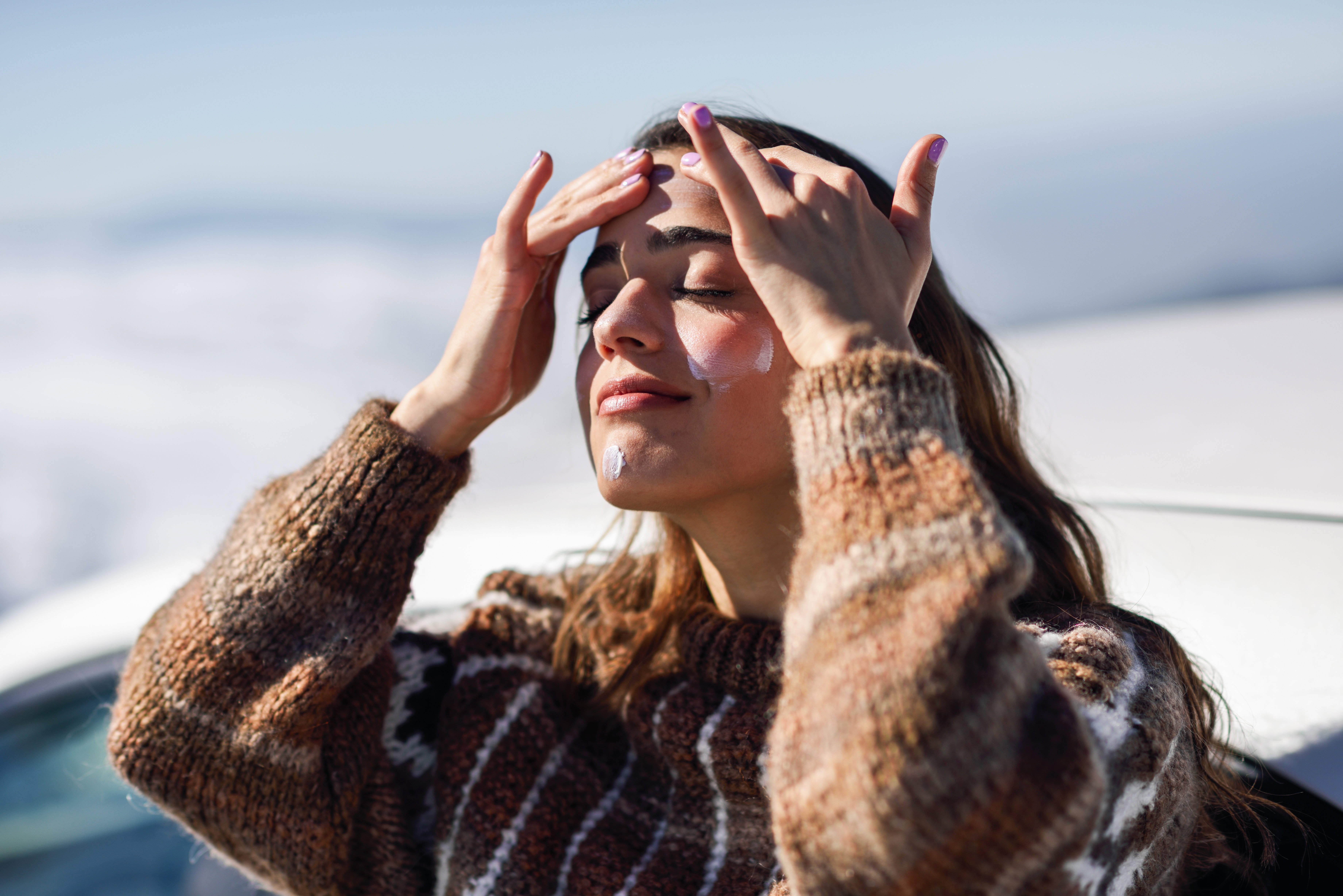 Young woman applying sunscreen on her face in snow landscape