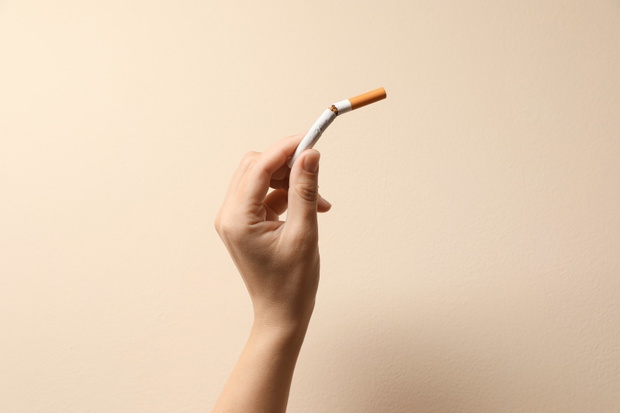 Stop smoking. Woman holding broken cigarette on beige background, closeup