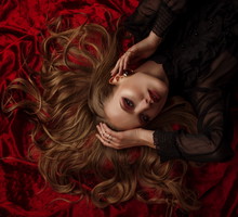 Beautiful lady with luxury blond hair, glow skin, dark red eyes and lips makeup, wearing a lot of golden rings, stylish earrings, posing, laying on velvet sheets. Close up studio portrait