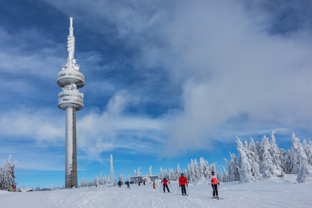 Calm sunny morning in ski resort Pamporovo.  Several people are skiing on white slopes near Snejanka TV tower.  Sports and recreation concept. Selective focus.