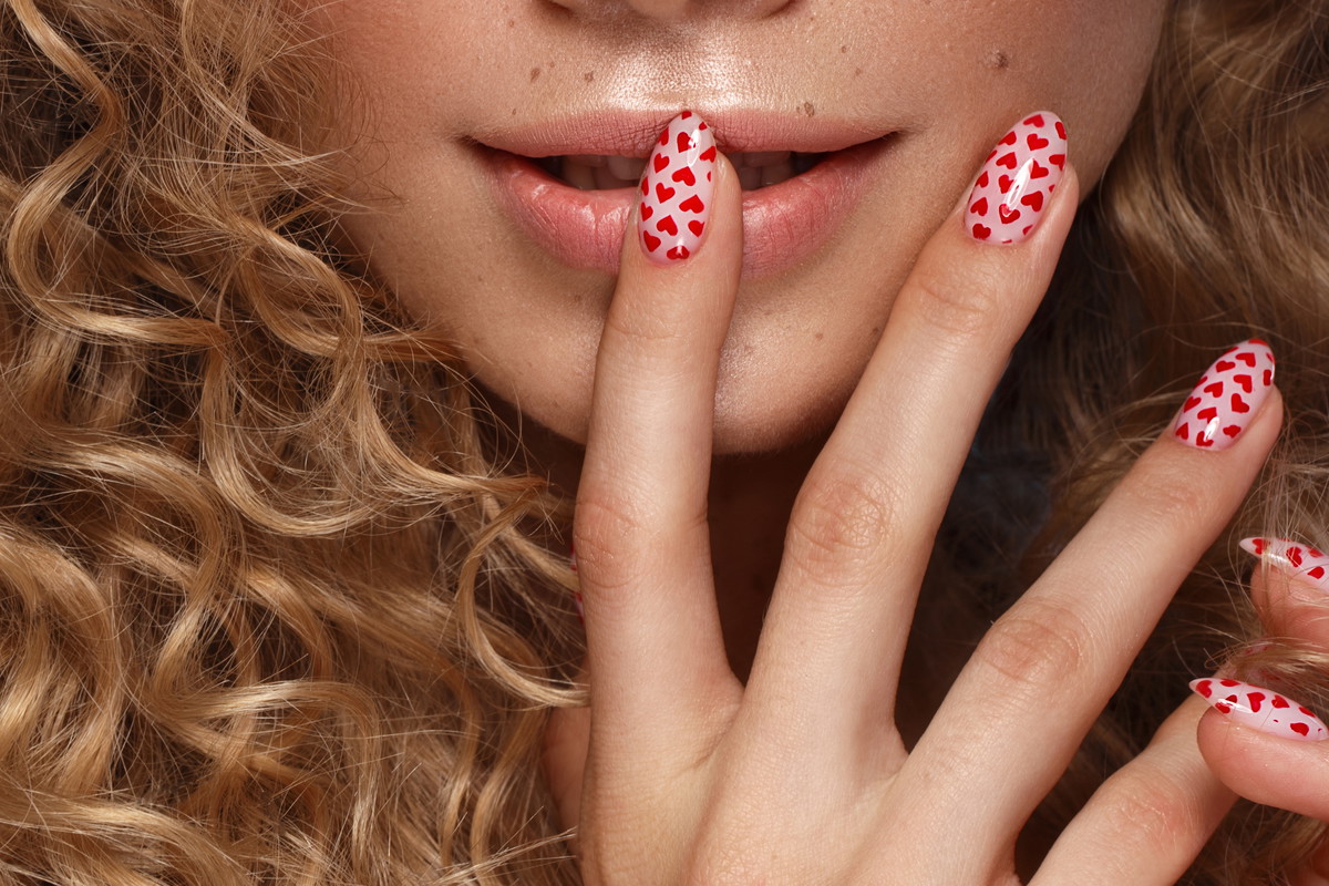 Pretty girl with curls hairstyle, classic makeup, freckles, nude lips and manicure design with hearts. Beauty face. The image for Valentine's Day