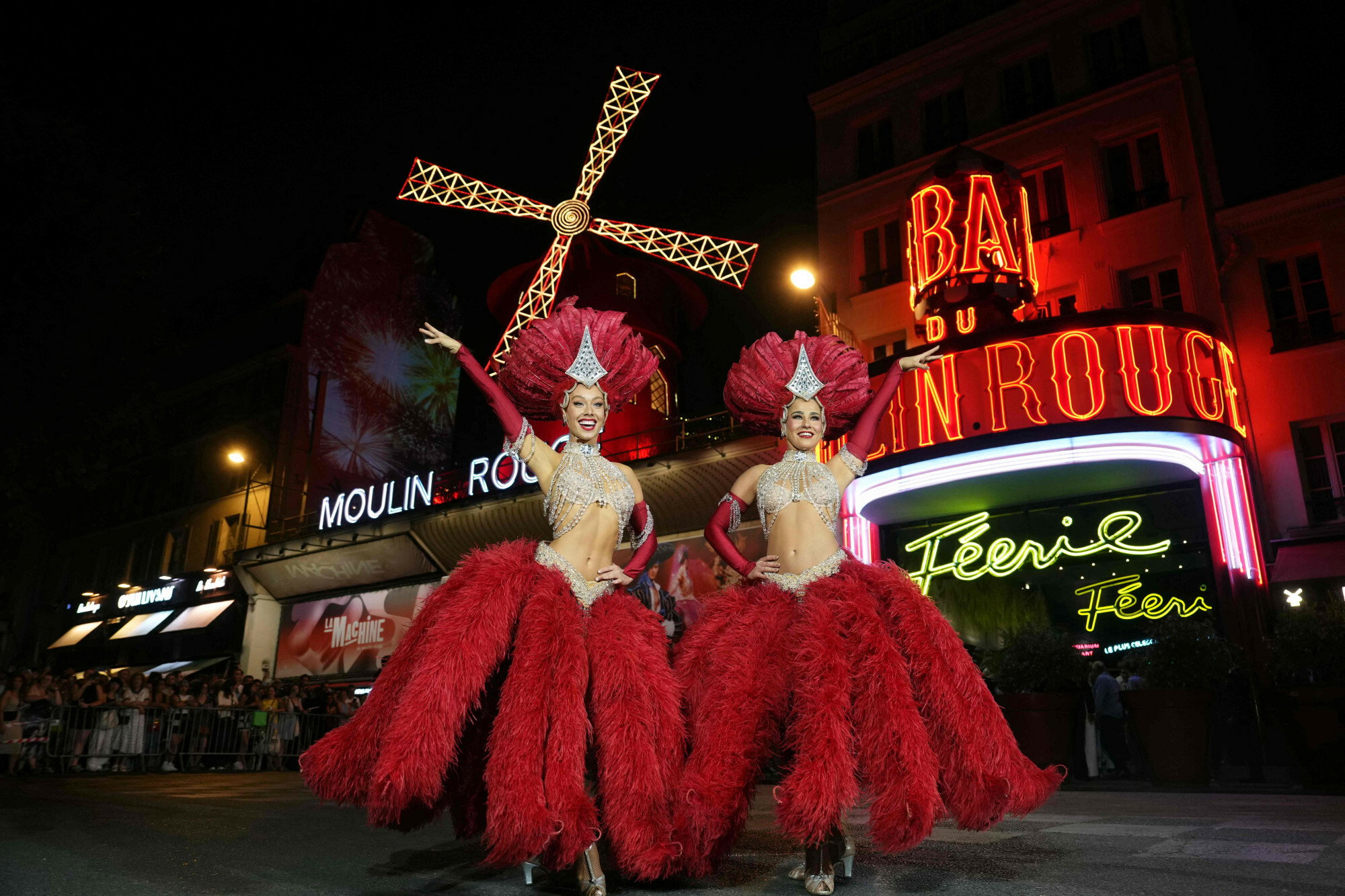 Moulin Rouge Can-can dancers pose underneath the new the sails of The Moulin Rouge Windmill in Paris on July 10, 2025. Fourteen months after their fall, the Moulin Rouge's wings have been reinstalled and are moving again, reviving a tradition spanning mor