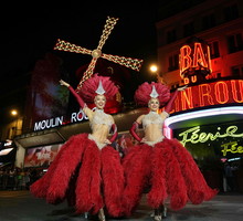 Moulin Rouge Can-can dancers pose underneath the new the sails of The Moulin Rouge Windmill in Paris on July 10, 2025. Fourteen months after their fall, the Moulin Rouge's wings have been reinstalled and are moving again, reviving a tradition spanning mor