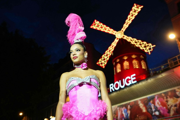 A Can-can dancer poses underneath the new the sails of The Moulin Rouge Windmill in Paris on July 10, 2025. Fourteen months after their fall, the Moulin Rouge's wings have been reinstalled and are moving again, reviving a tradition spanning more than 135