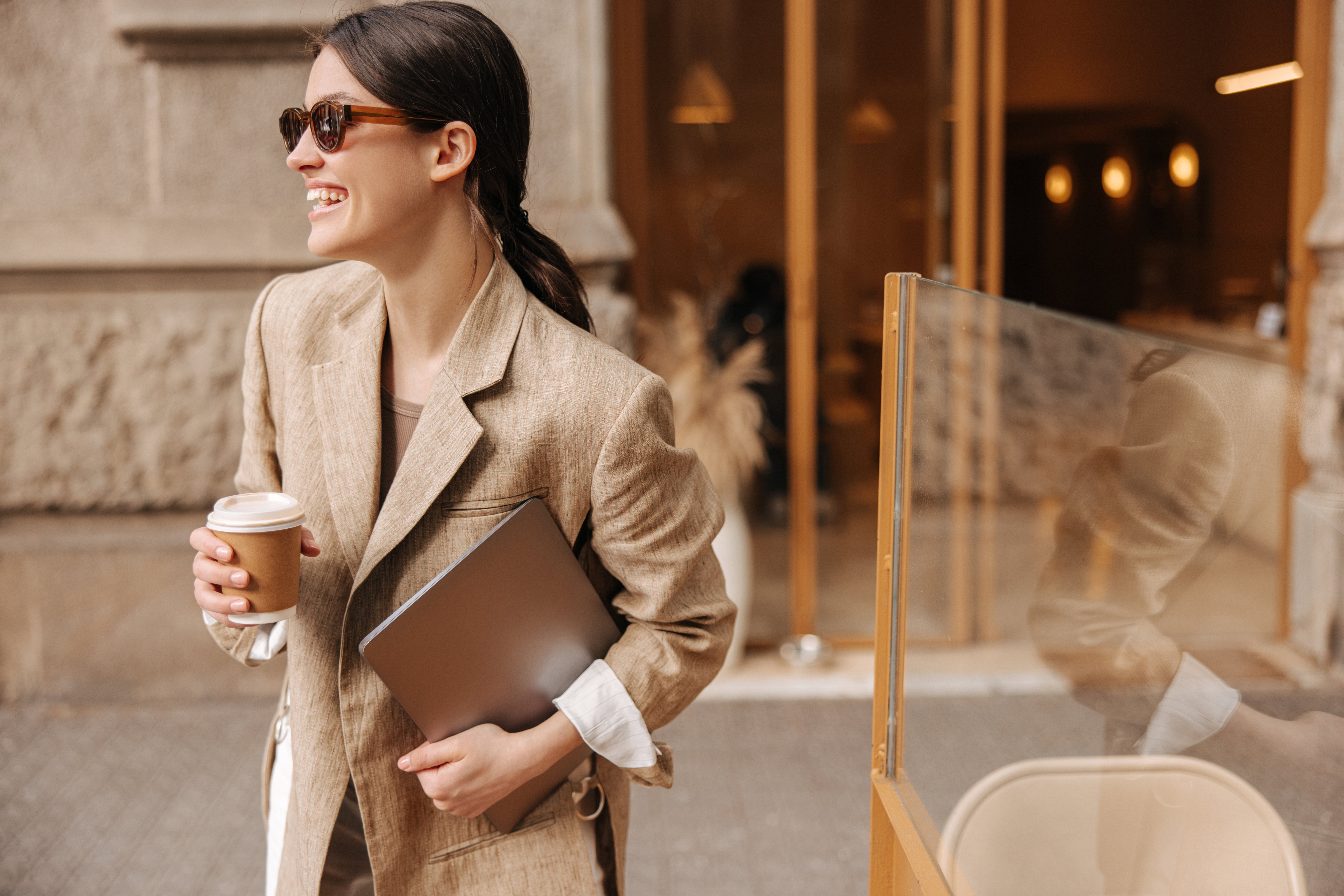 Happy young caucasian brunette woman with laptop and coffee posing outdoors.