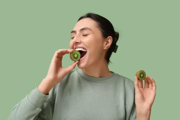 Beautiful young woman with tasty kiwi on green background