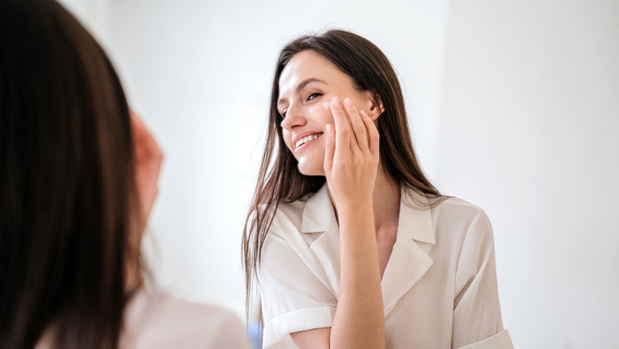 Happy female apply anti aging moisturizing cosmetic cream on face