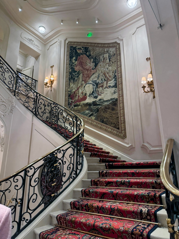 Wnętrze paryskiego Hotelu Ritz, widok na kultowe schody z czerwonym dywanem i ozdobnym gobelinem.