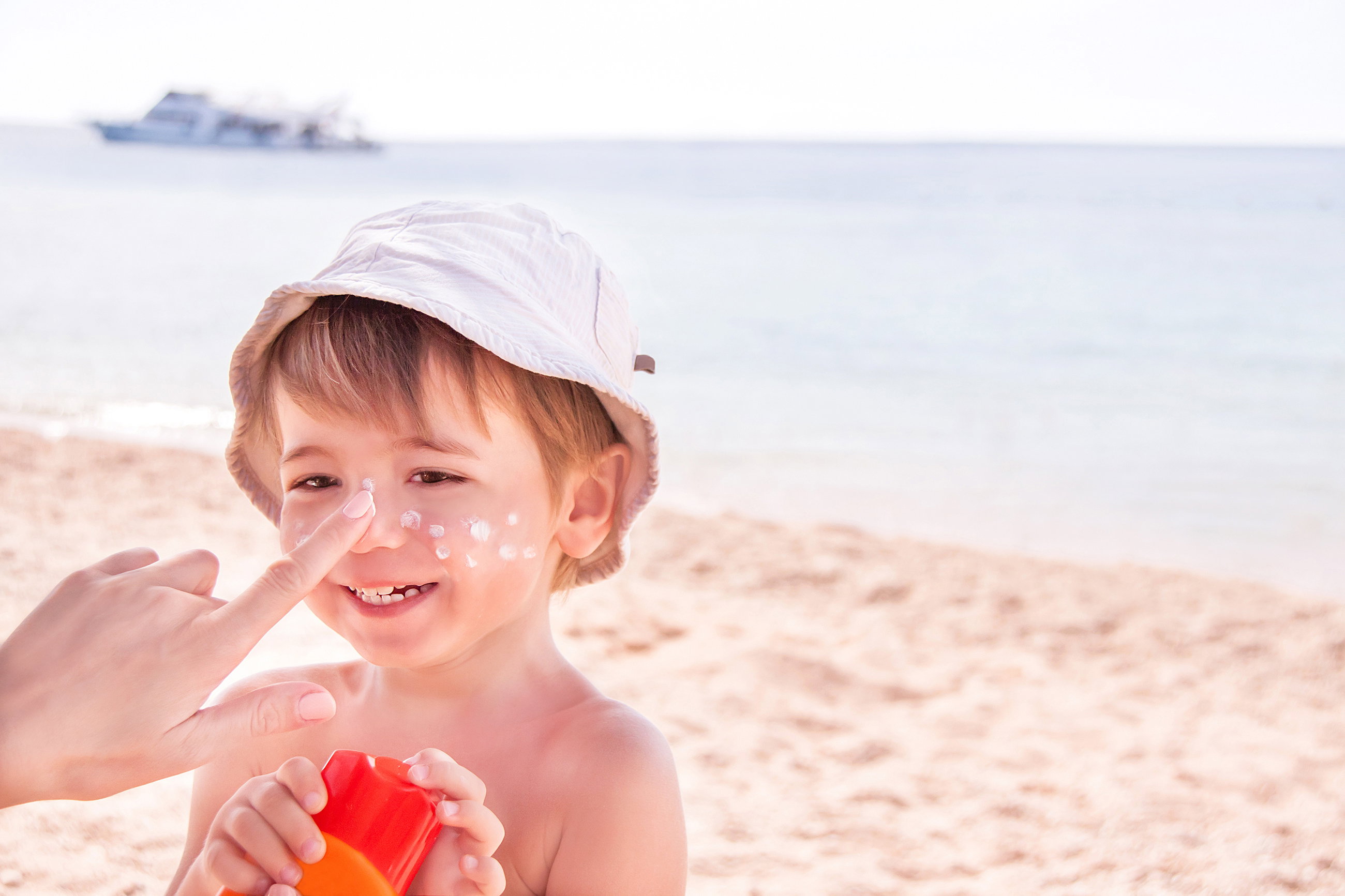 Dziecko na plaży, które ma aplikowany na nos krem przeciwsłoneczny