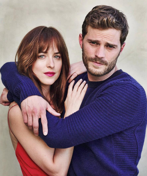 Dakota Johnson w czerwonej sukience jest obejmowana przez Jamiego Dornana w granatowym swetrze