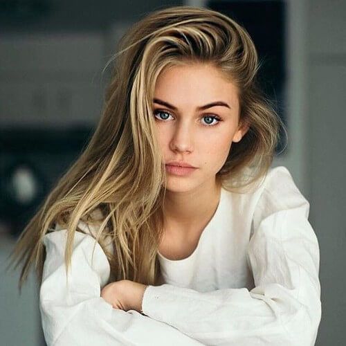 Dziewczyna z długimi blond włosami siedzi na krzesełku w białej koszuli