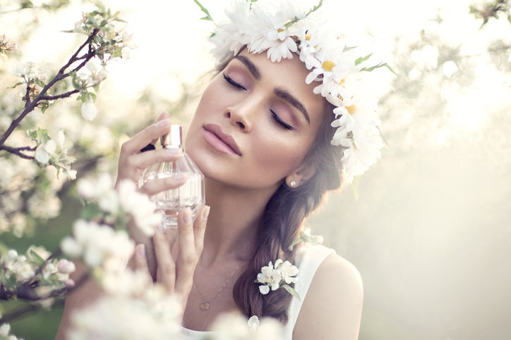 Kobieta z wiankiem w brązowych włosach na tle kwiatów wącha perfumy