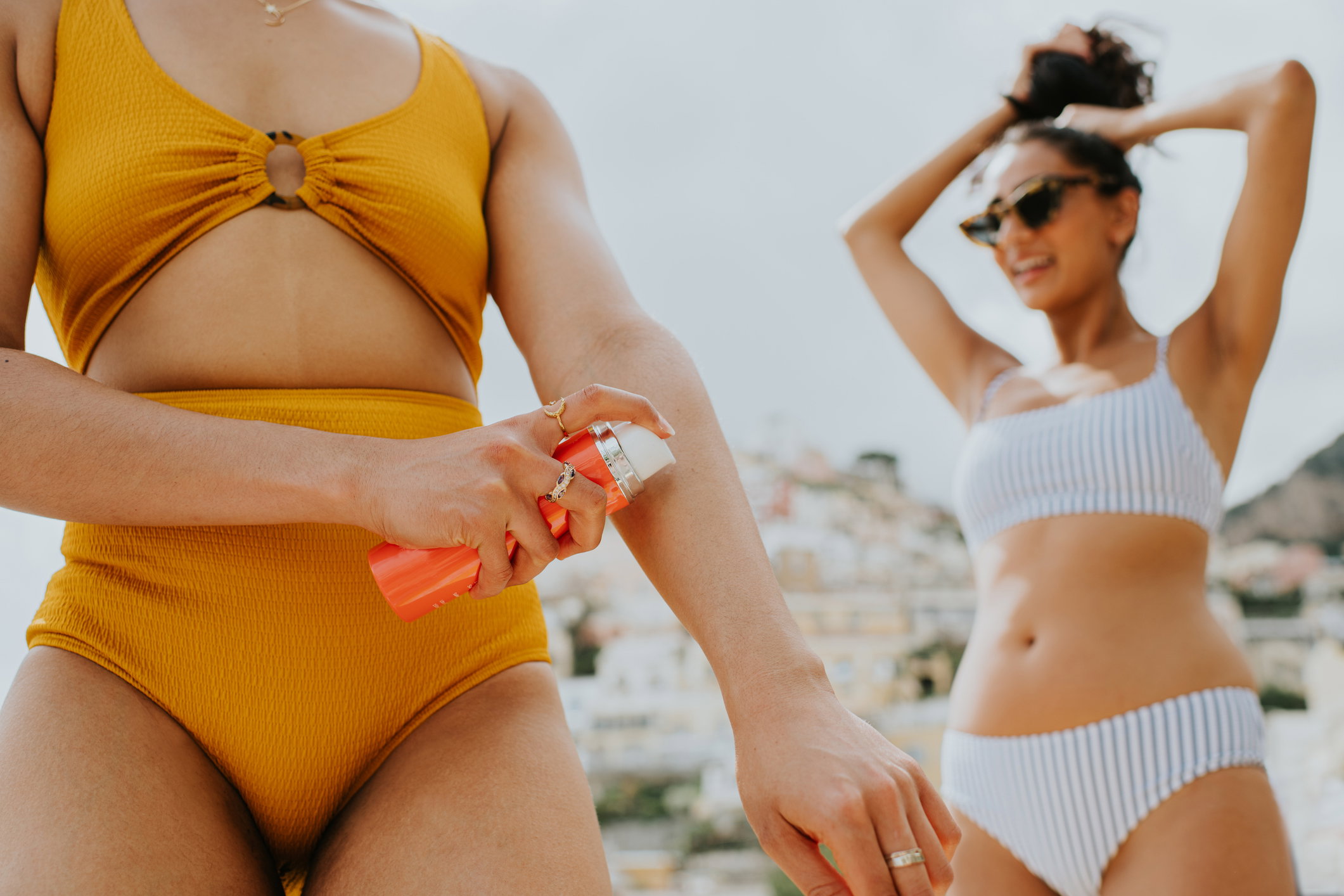 Two woman prepare for a beach day by applying suncream and tying hair back