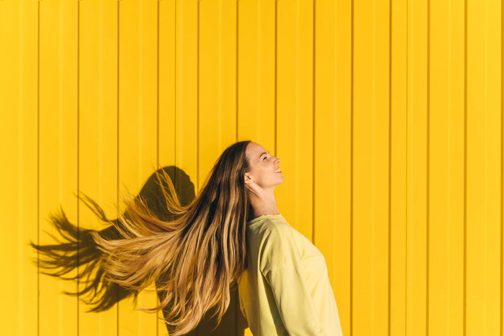 Woman with flying hair in yellow sweatshirt on yellow wall background.
