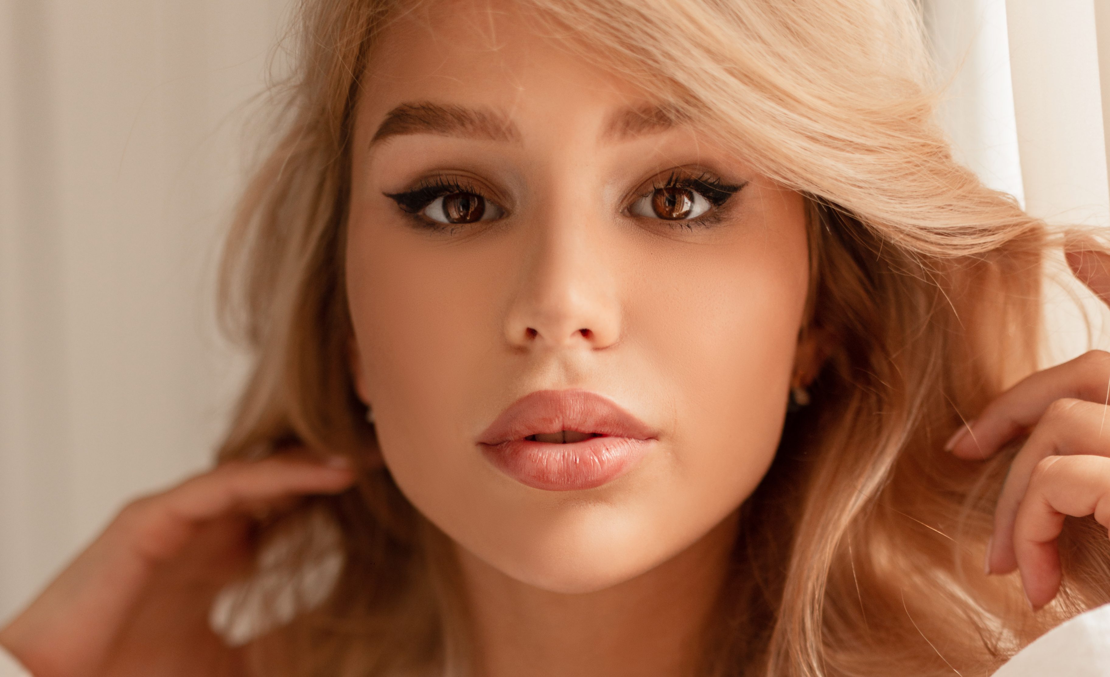 Adorable female portrait of a beautiful young blonde woman with a cute face in a white linen shirt indoors. Lovely girl looking at the camera