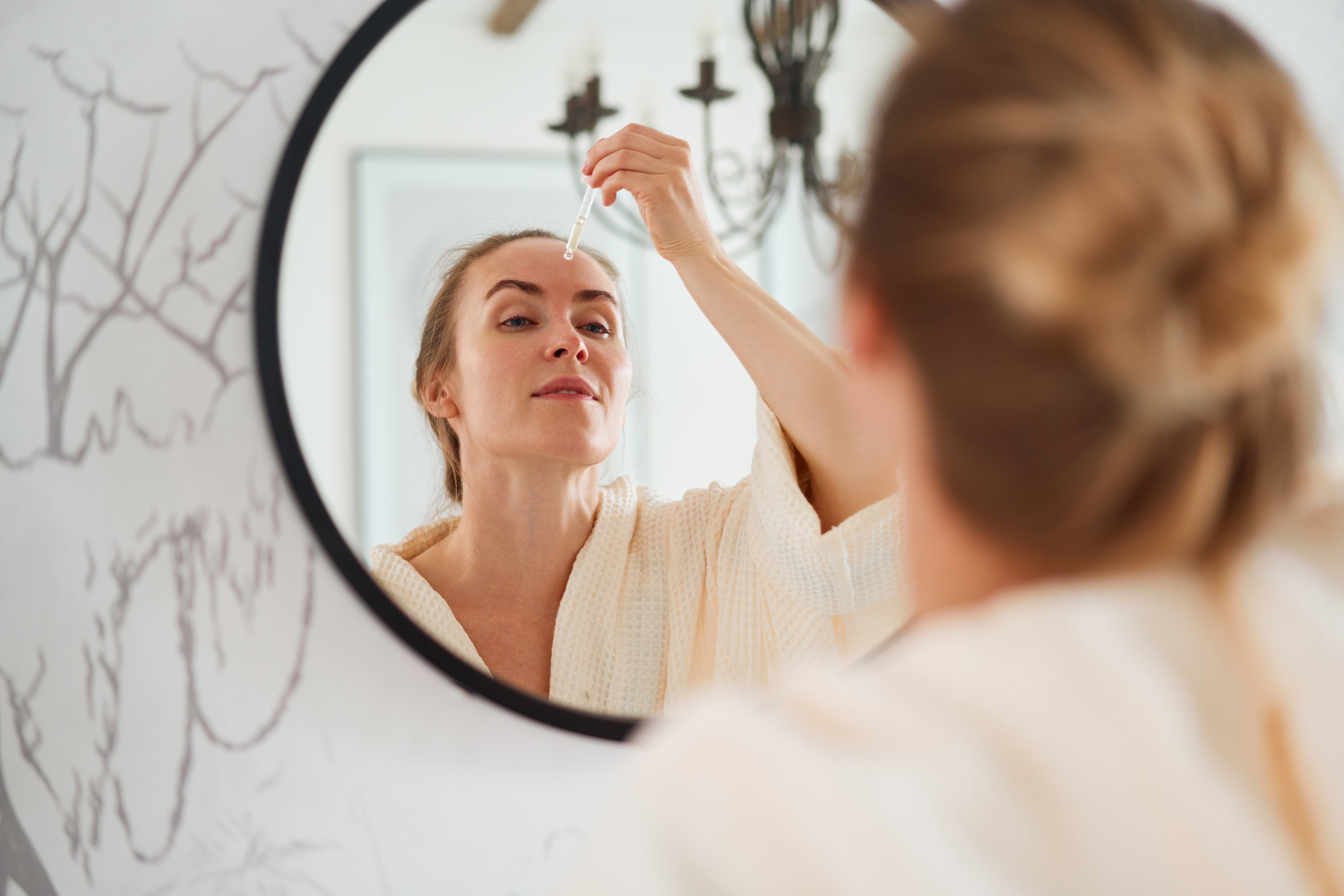 kobieta nakładająca przed lustrem serum na twarz