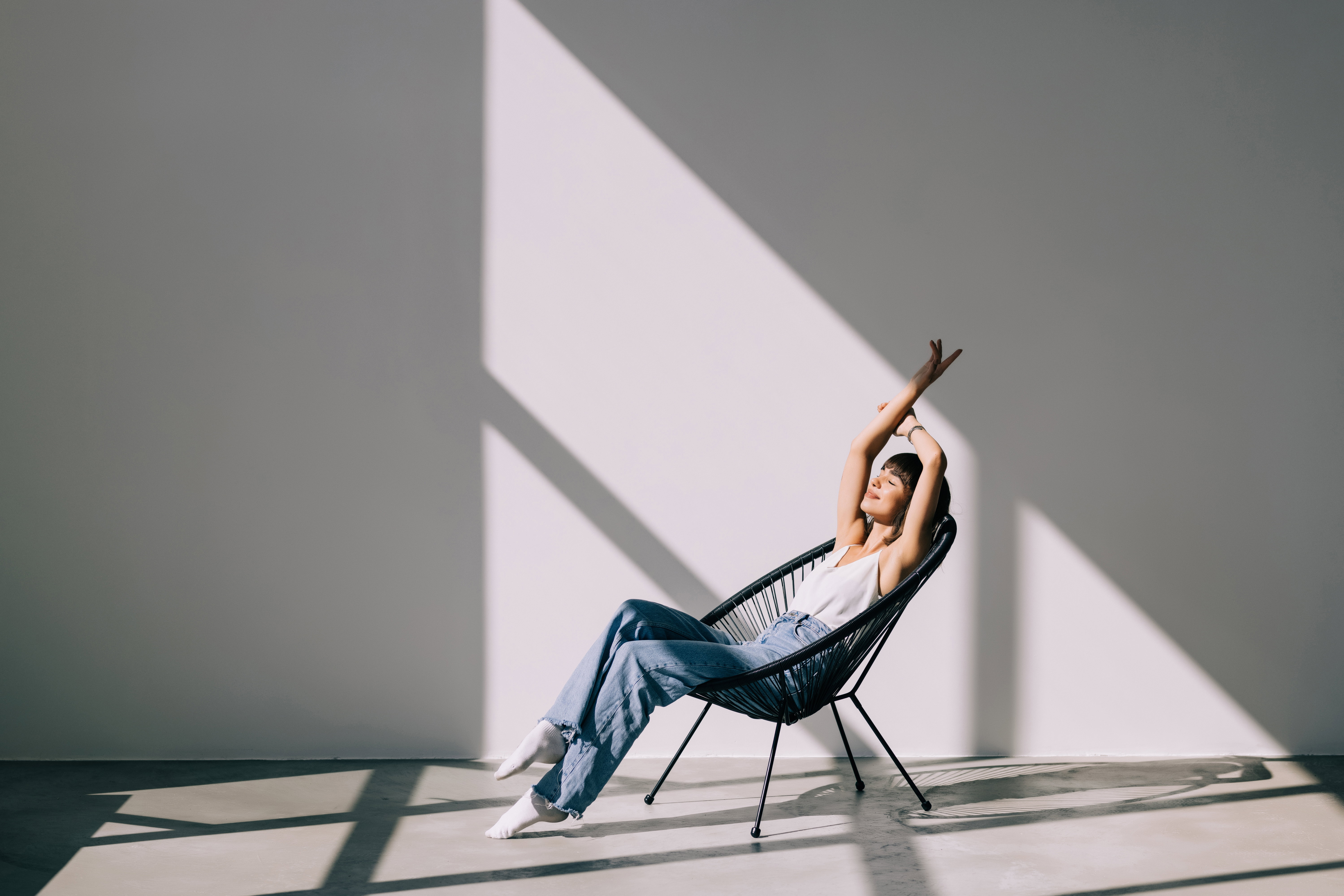 Young woman at home sitting on modern chair in front of window relaxing in her living room